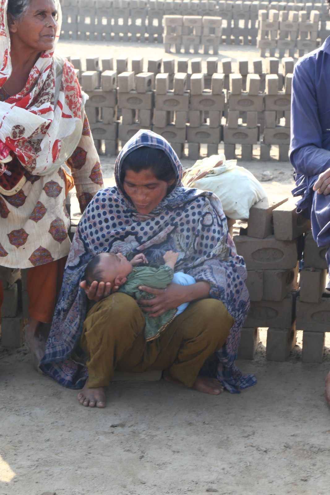 A young mother holding her baby, with an elder from the community nearby